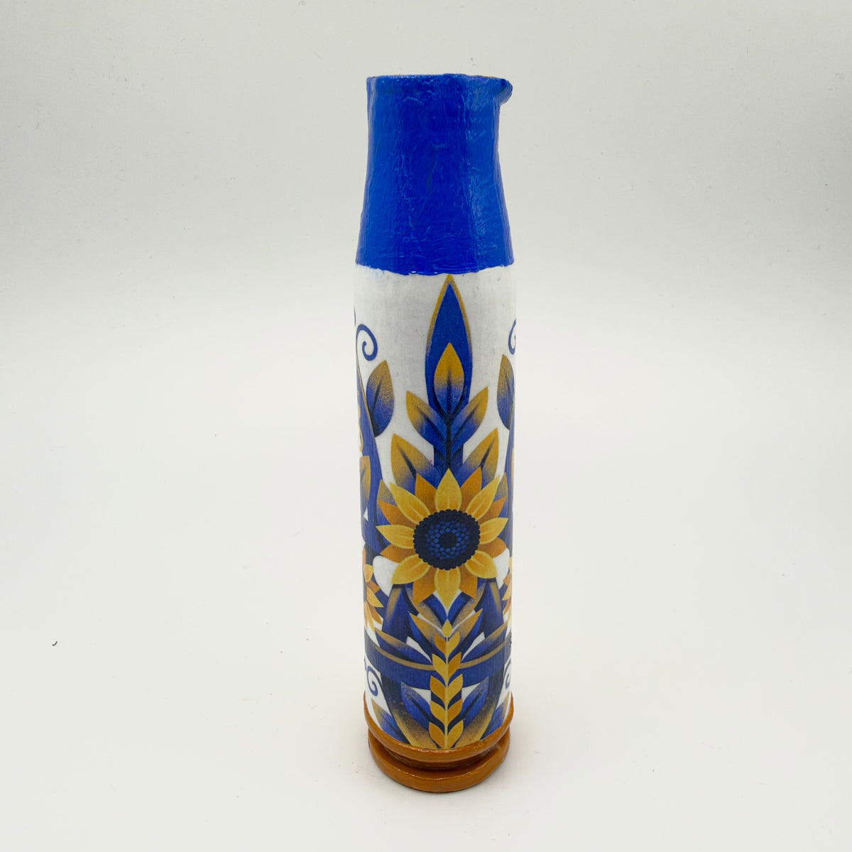 Decorated shell casing with a vivid blue neck and golden-brown base, featuring a yellow sunflower surrounded by blue and gold foliage on a white background.