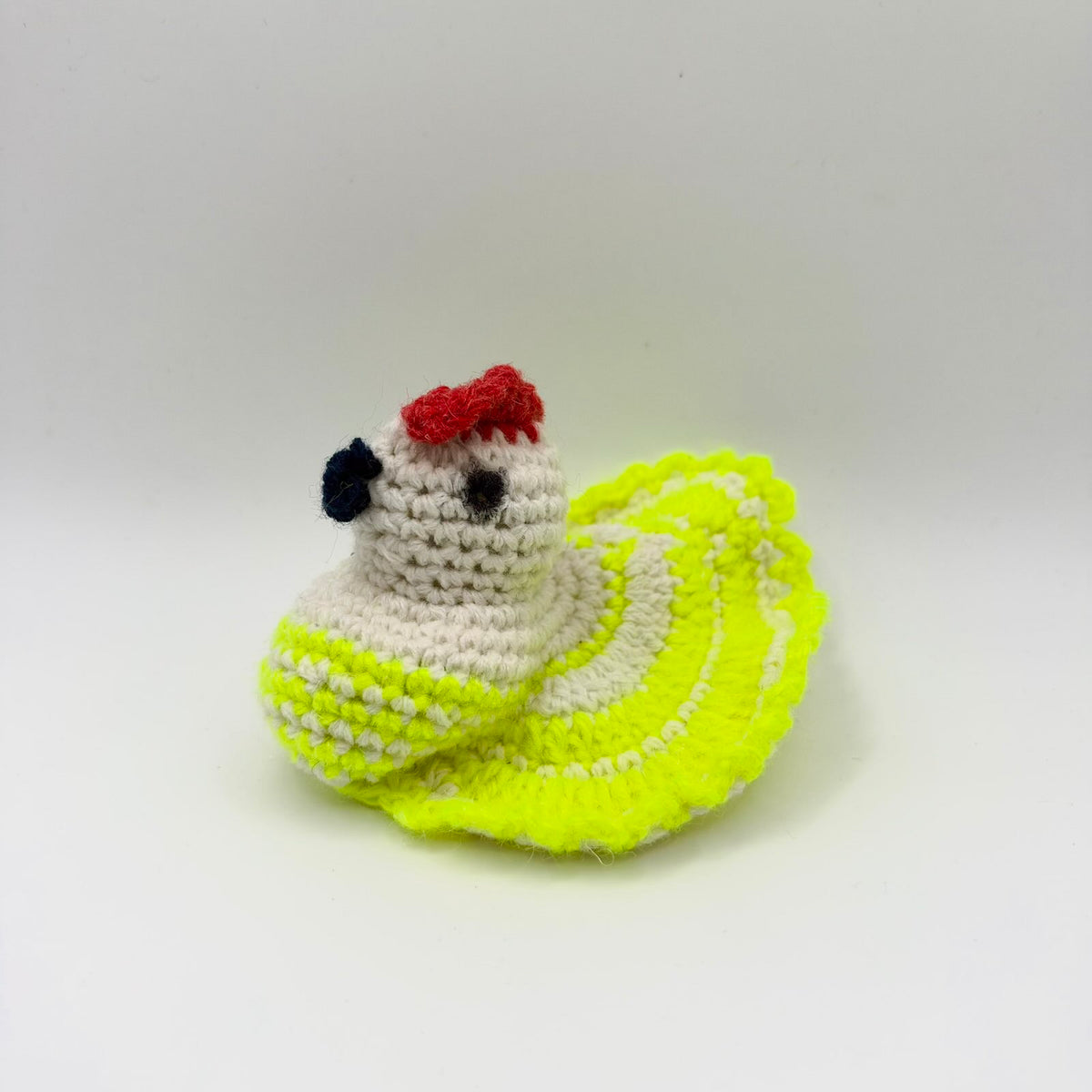 Crochet hen-shaped egg warmer with a cream head and neck, red comb, dark beak and dark stitched eye. Its vivid yellow and cream body has patterned wings and a broad, upright fan-shaped tail with scalloped edging. Photographed from the side against a plain light background.