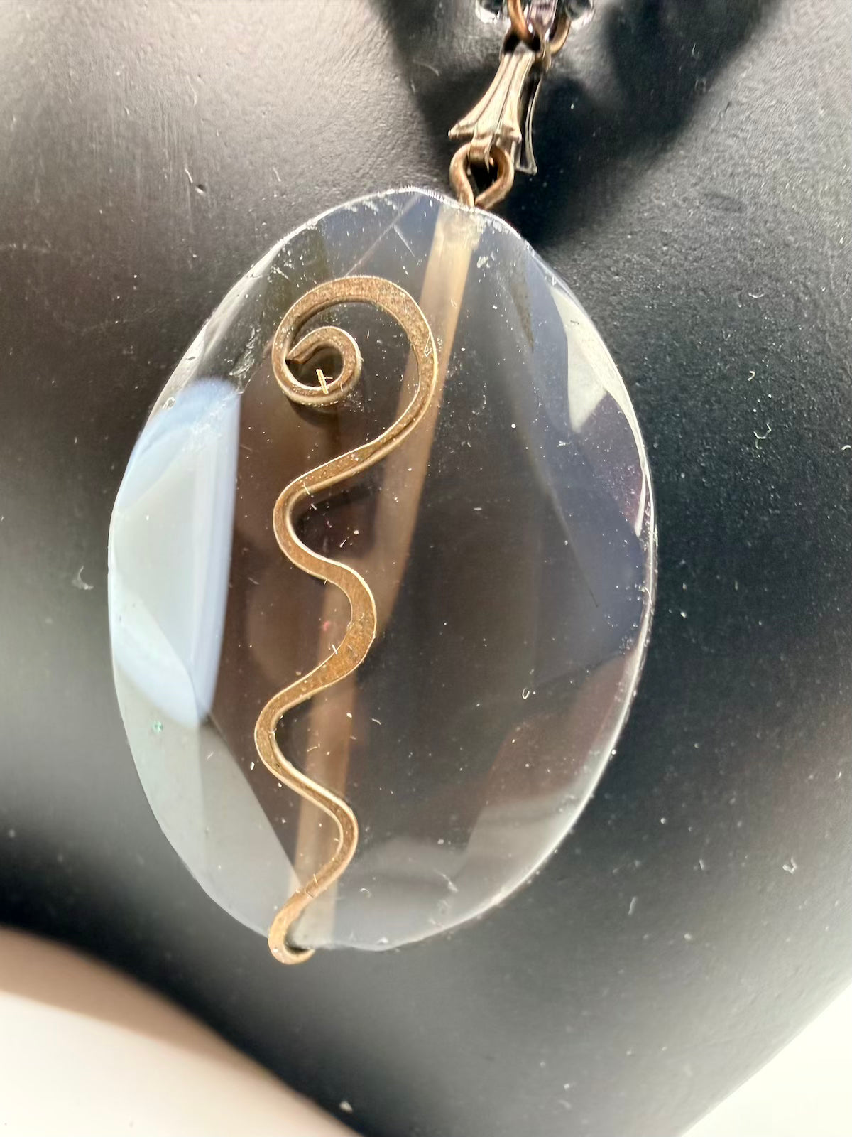 Pendant with a gold spiral design on a clear stone against a dark background