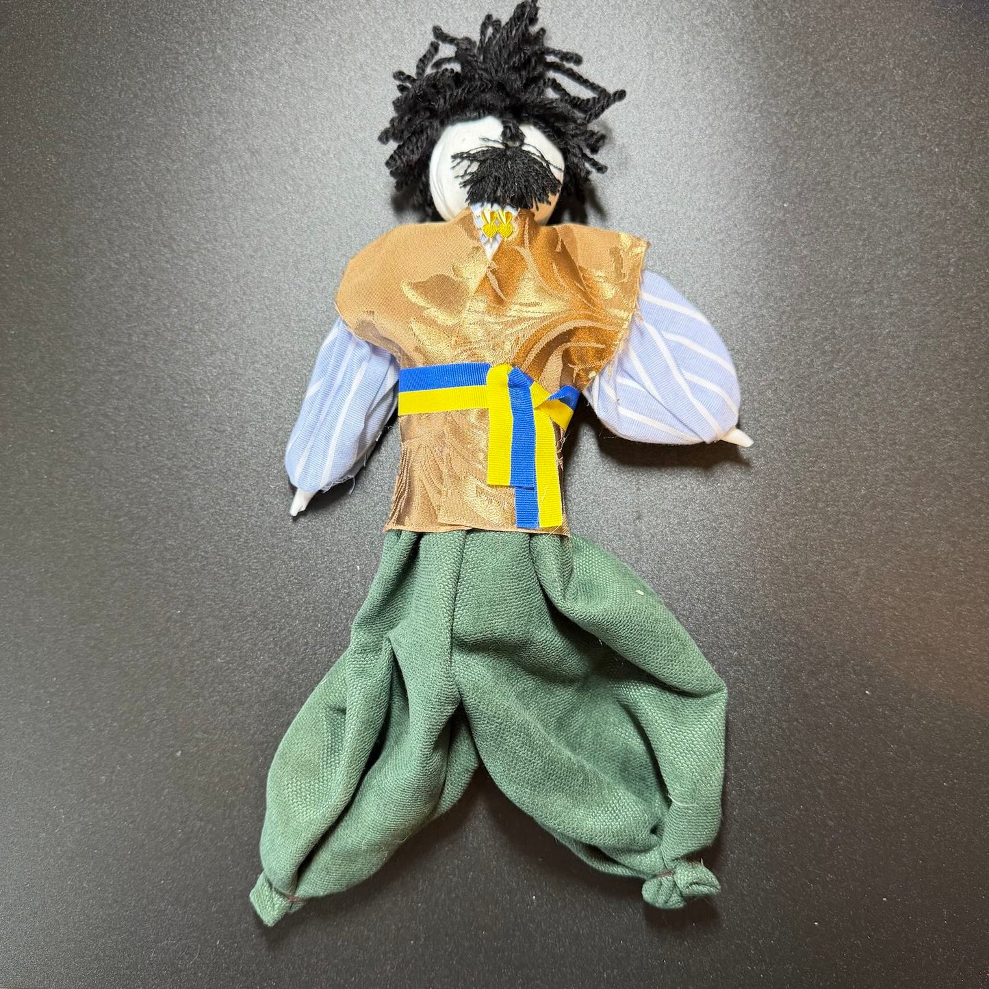 Handmade doll with green pants and a brown top on a gray background