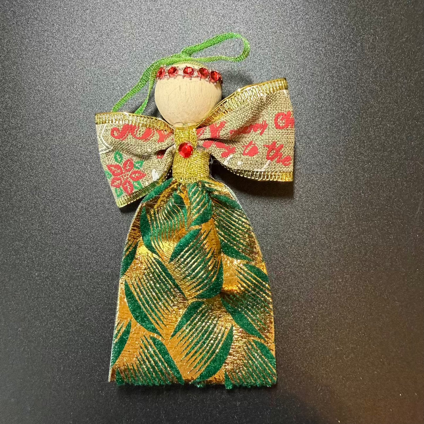 Decorative angel ornament with gold and green fabric and red berries on a dark background