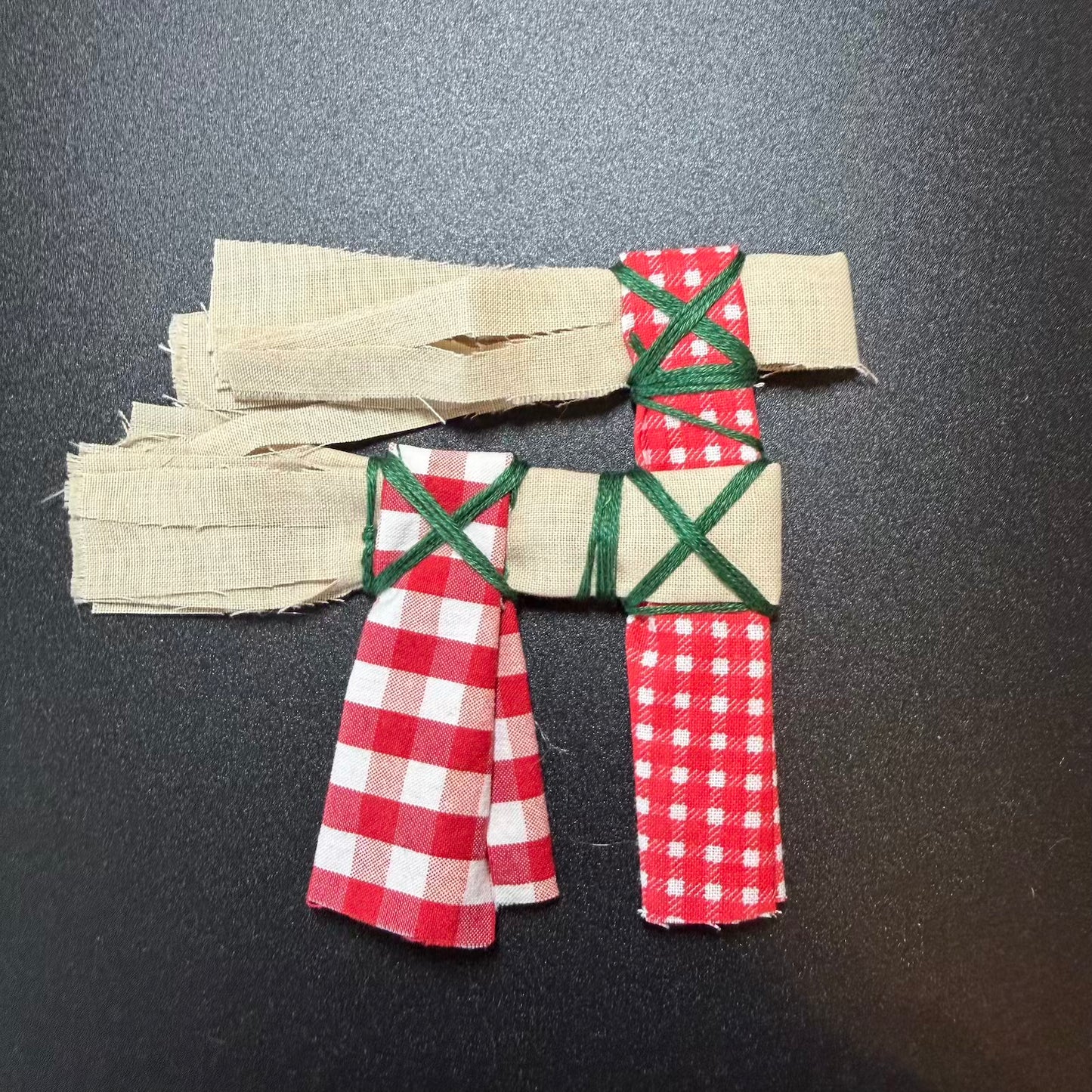 Fabric letter 'F' with red and green checkered pattern on a dark background