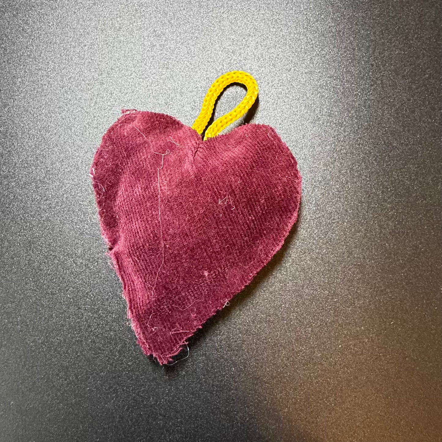 Heart-shaped fabric item with a yellow loop on a metallic surface