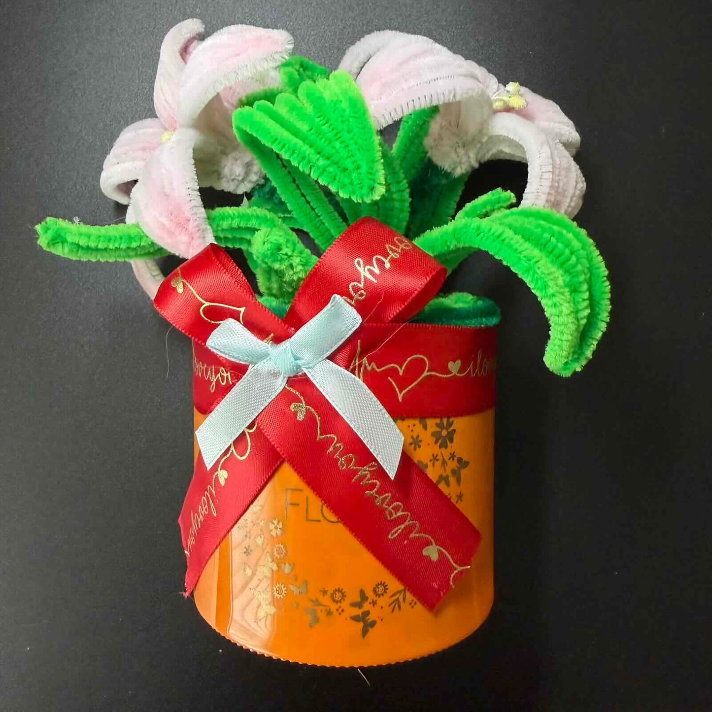 Artificial flower arrangement in a decorative pot with ribbons on a dark background