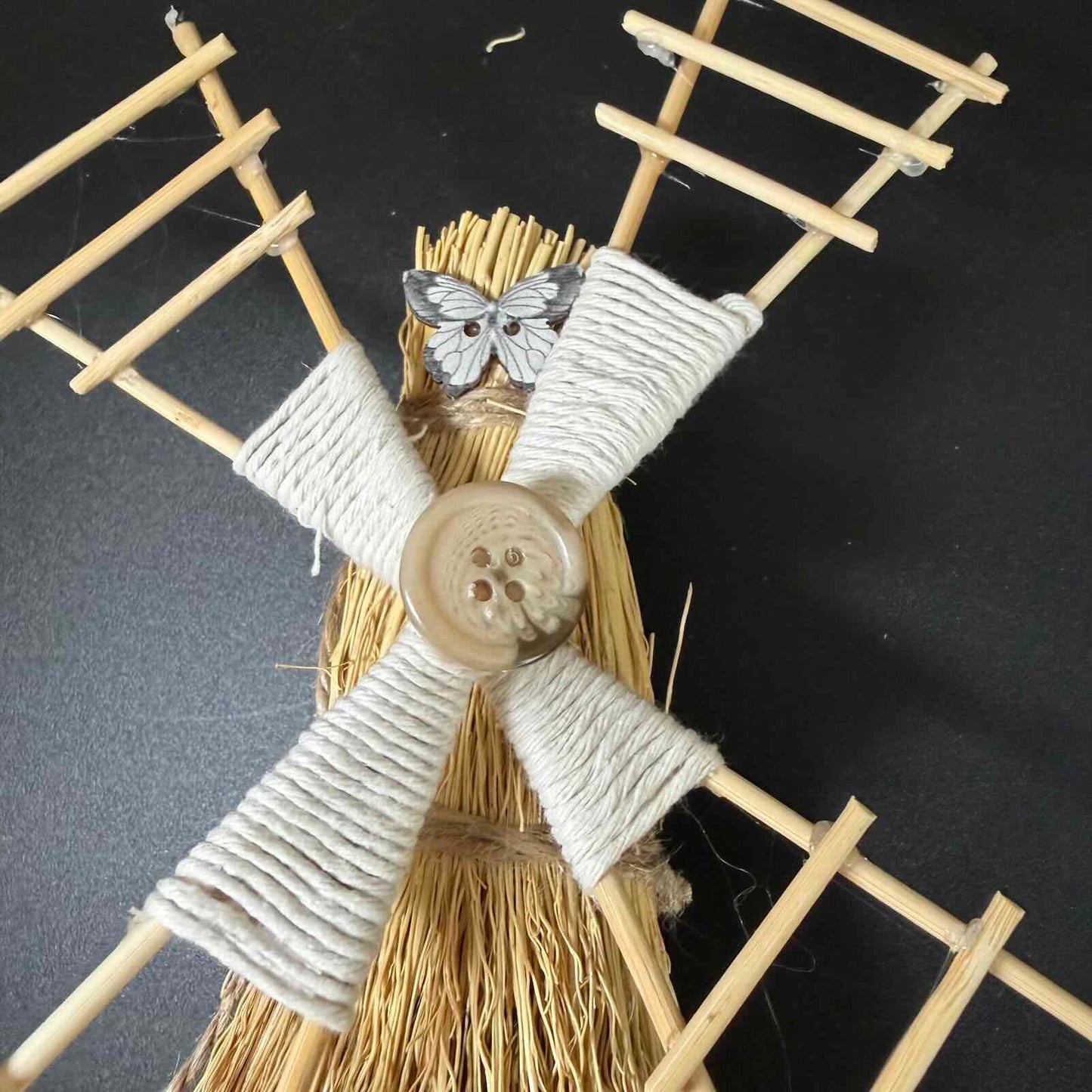 Decorative broom with woven handles and a button on a dark background