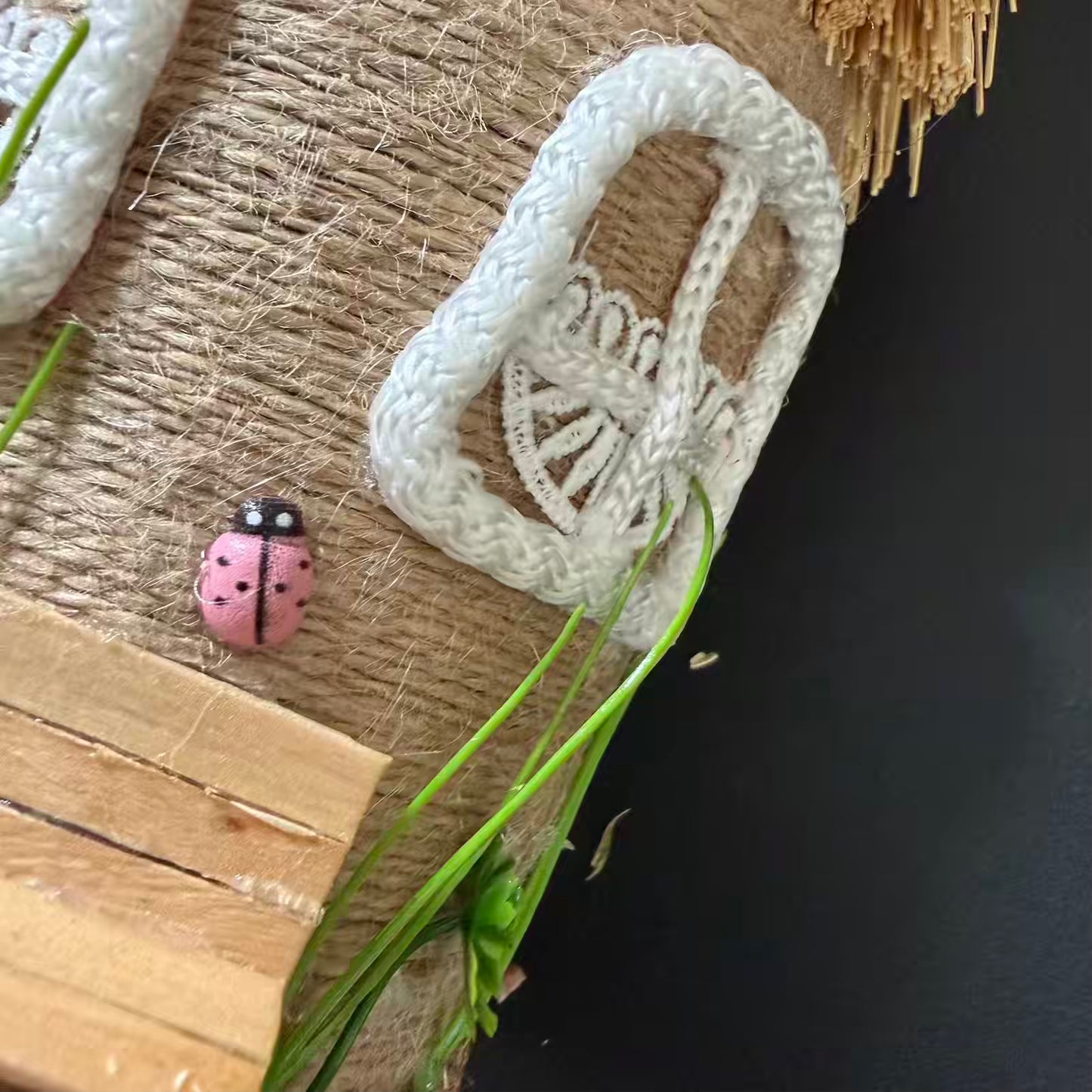 White crocheted item on a textured surface with a pink ladybug and green leaves.
