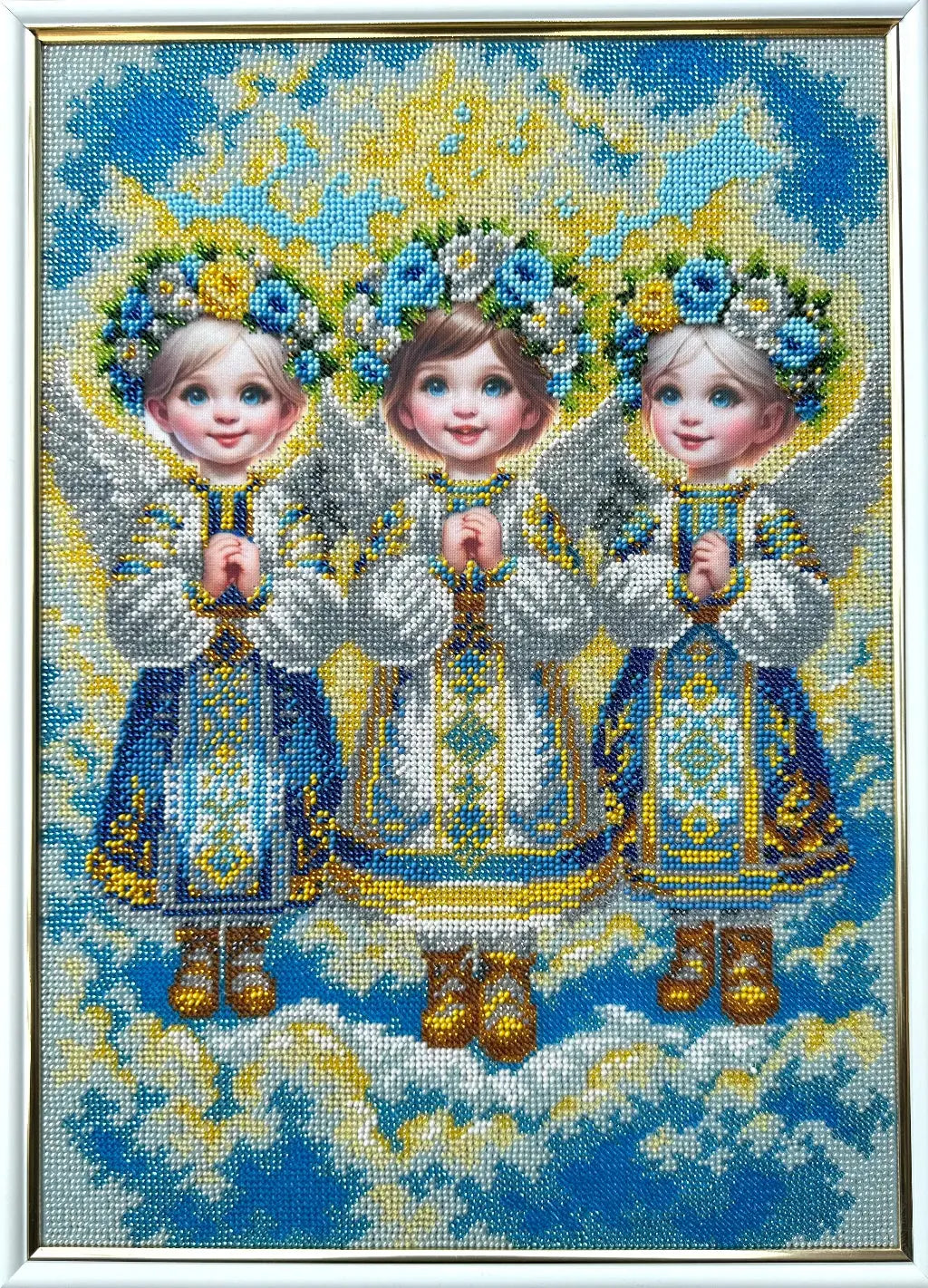 Cross-stitched depiction of three children in traditional attire with floral crowns against a blue sky.