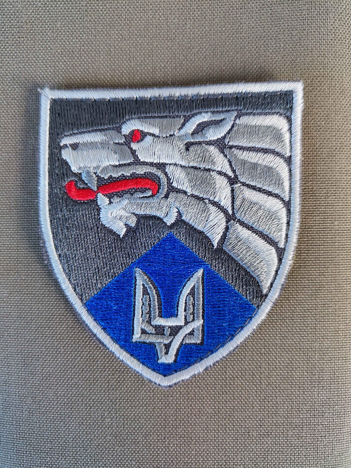 Fabric patch depicting a Wolves head in silver with a red tongue. Underneath is a Ukrainian Trident symbol