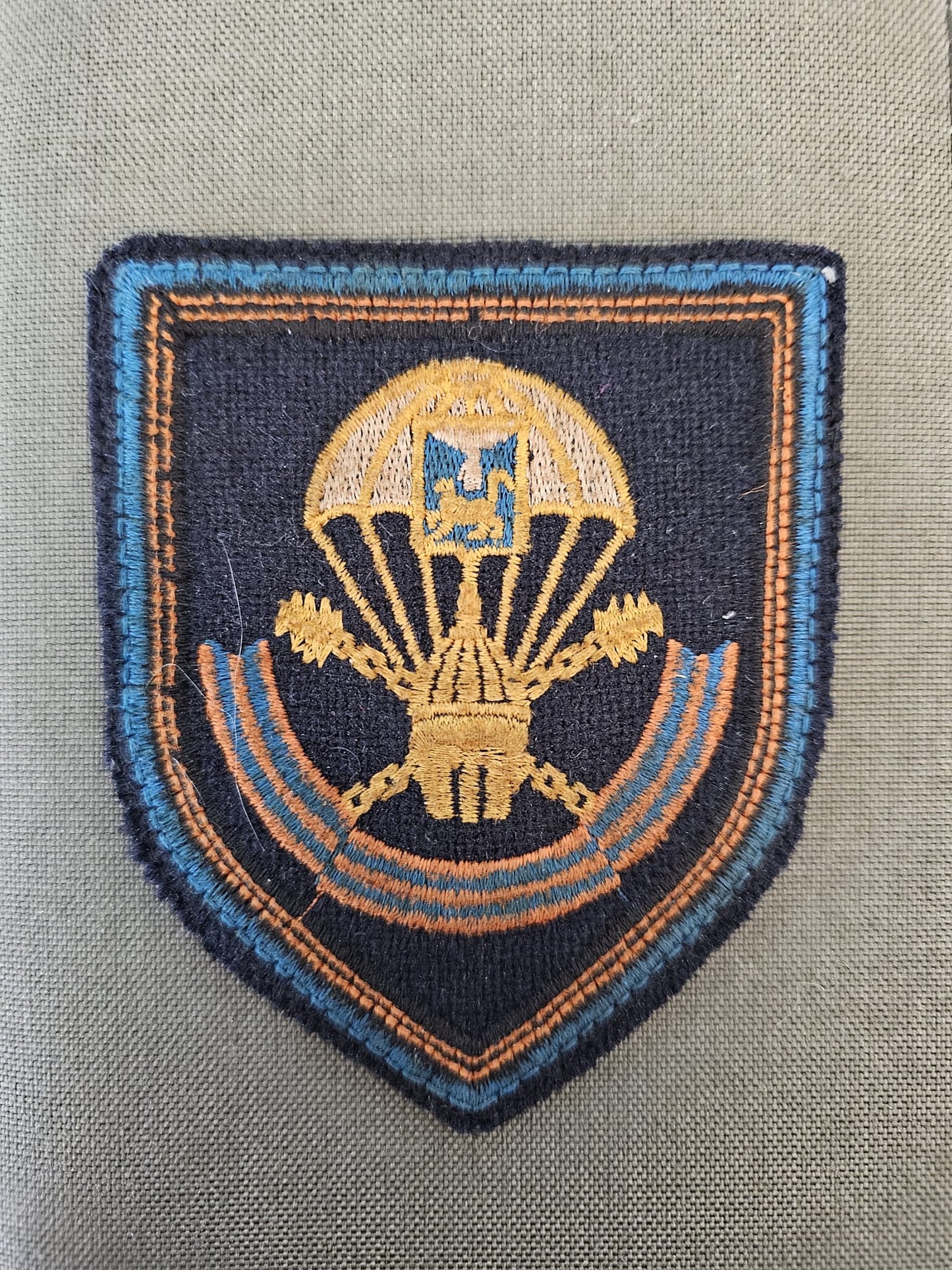 Fabric patch showing a golden parachute depending over the blue and yellow ribbon.
