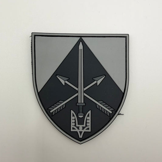 Grey and black shield-shaped patch featuring an upright sword over crossed arrows, with a stylised two-pronged emblem at the base.