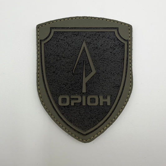 Olive and black Orion shield patch with a central spear-like emblem, Ukrainian “ОРІОН” lettering, textured background, and stitched outer border.