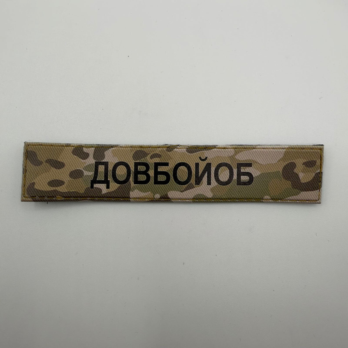 Long rectangular camouflage patch with bold black Ukrainian text “ДОВБОЙОБ” and a tan stitched border.