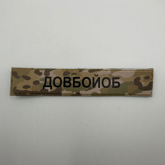 Long rectangular camouflage patch with bold black Ukrainian text “ДОВБОЙОБ” and a tan stitched border.