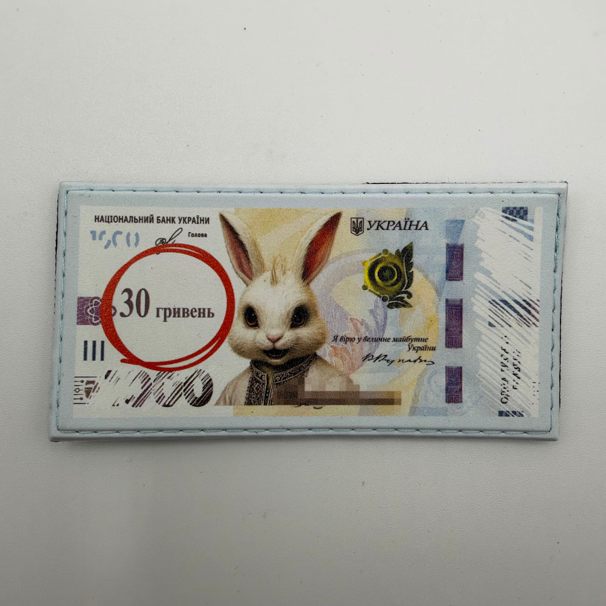 Banknote-style patch featuring a white hare in an embroidered shirt, “30 гривень” inside a red circle, and a pale blue stitched border.