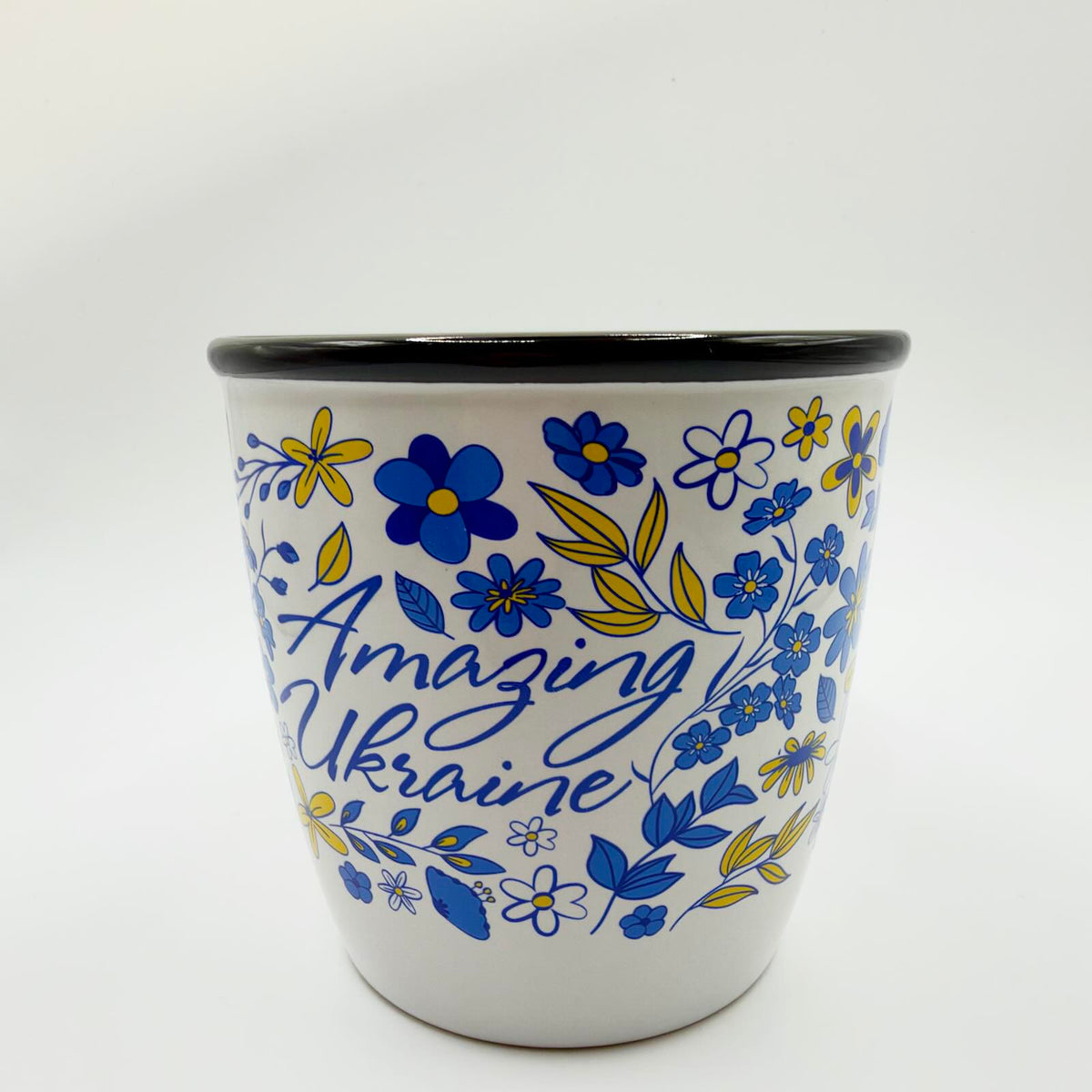 White mug with a black rim, decorated with blue and yellow flowers and leaves surrounding blue “Amazing Ukraine” lettering.