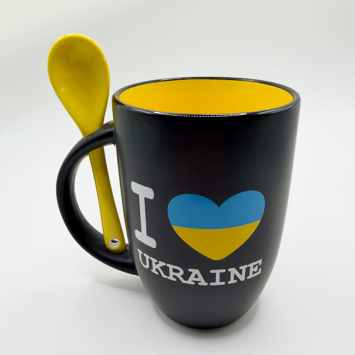 Black “I Love Ukraine” mug with a blue and yellow heart, yellow interior and matching yellow spoon slotted upright into the handle.