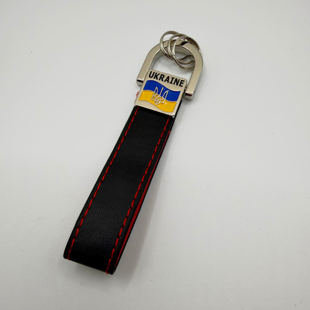 Black strap keyring with red stitching, silver-tone rings and a badge featuring UKRAINE lettering, a blue and yellow flag and a Tryzub.