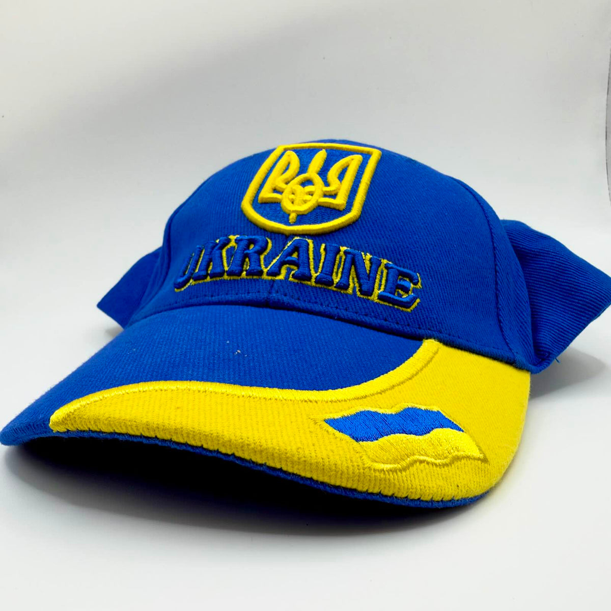 Blue and yellow Ukraine baseball cap with an embroidered shield emblem, UKRAINE lettering and a Ukrainian flag on the curved peak.