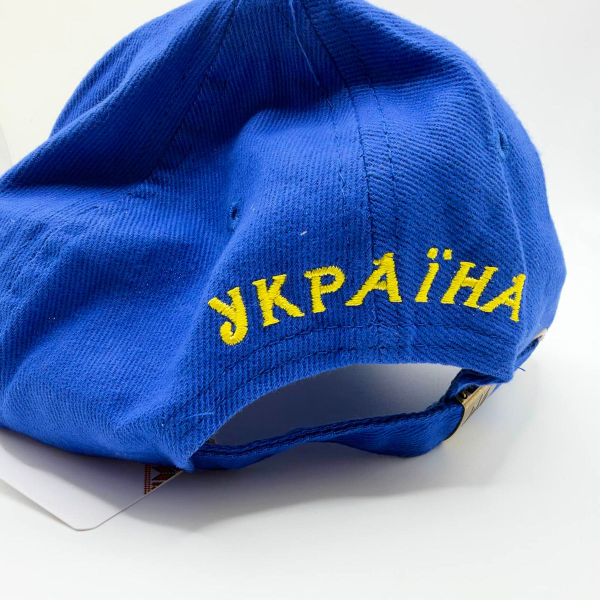 Rear view of the blue Ukraine cap showing yellow “УКРАЇНА” embroidery and an adjustable blue strap with a metal clasp.
