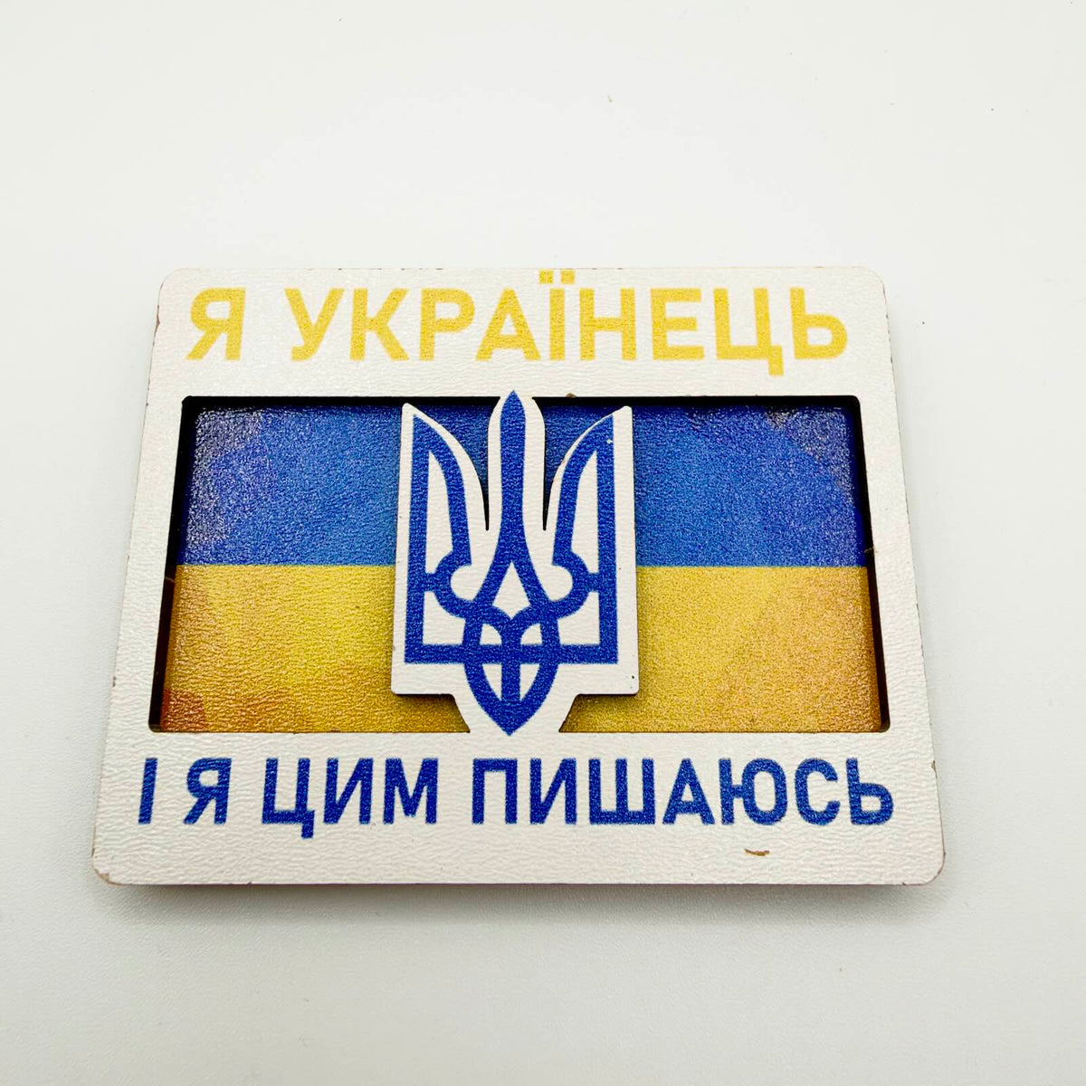 Layered fridge magnet with a raised blue Tryzub over the Ukrainian flag and Ukrainian text meaning “I am Ukrainian, and I am proud of it”.