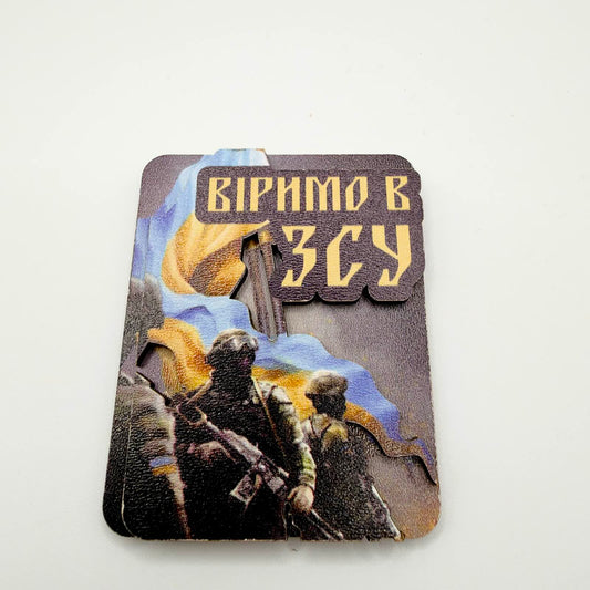 Layered rectangular fridge magnet showing Ukrainian soldiers beneath a blue and yellow flag, with Ukrainian text meaning “We believe in the Armed Forces of Ukraine”.