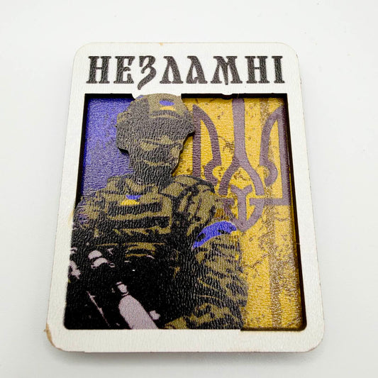 Layered fridge magnet showing a Ukrainian soldier against a blue and yellow background with a Tryzub and the Ukrainian word “Unbreakable” above.