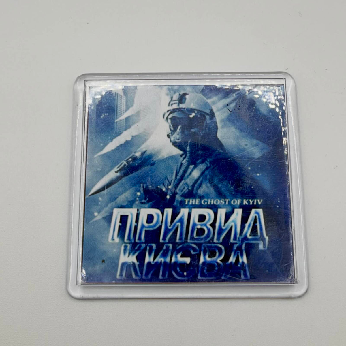 Blue-toned fridge magnet in a clear casing, featuring a helmeted pilot, fighter aircraft and “The Ghost of Kyiv” lettering in English and Ukrainian.