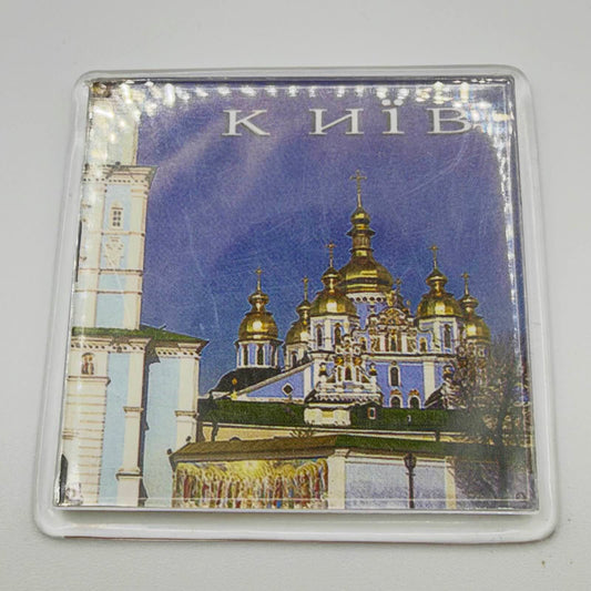 Kyiv souvenir fridge magnet in a clear casing, showing a blue-and-white cathedral with golden domes, a bell tower and “Київ” lettering.