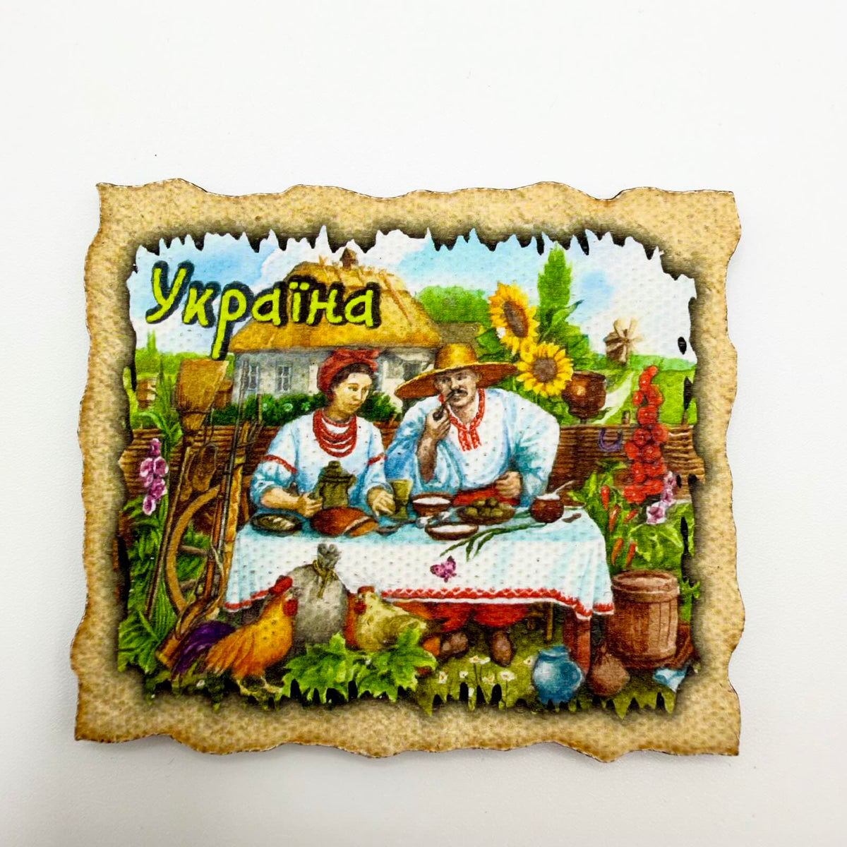 Ukrainian souvenir fridge magnet depicting a couple sharing a meal outside a thatched cottage, with sunflowers, chickens and a parchment-style border.