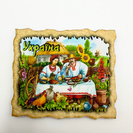 Ukrainian souvenir fridge magnet depicting a couple sharing a meal outside a thatched cottage, with sunflowers, chickens and a parchment-style border.