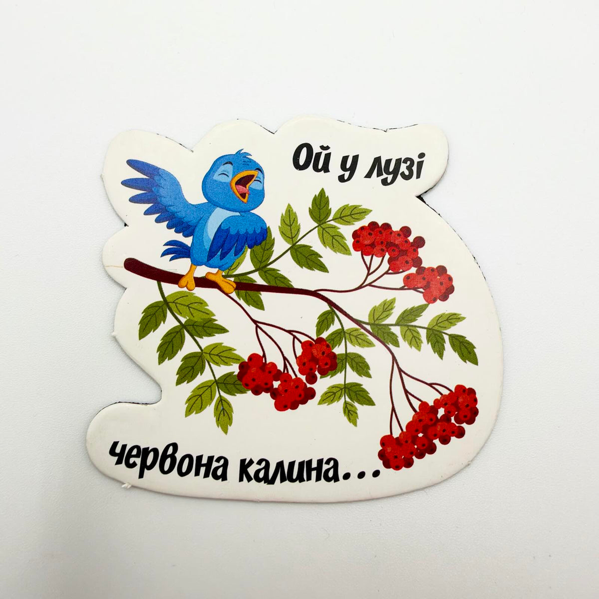 Shaped fridge magnet showing a singing blue bird on a leafy branch with red berries and Ukrainian text reading “Oi u luzi chervona kalyna…”
