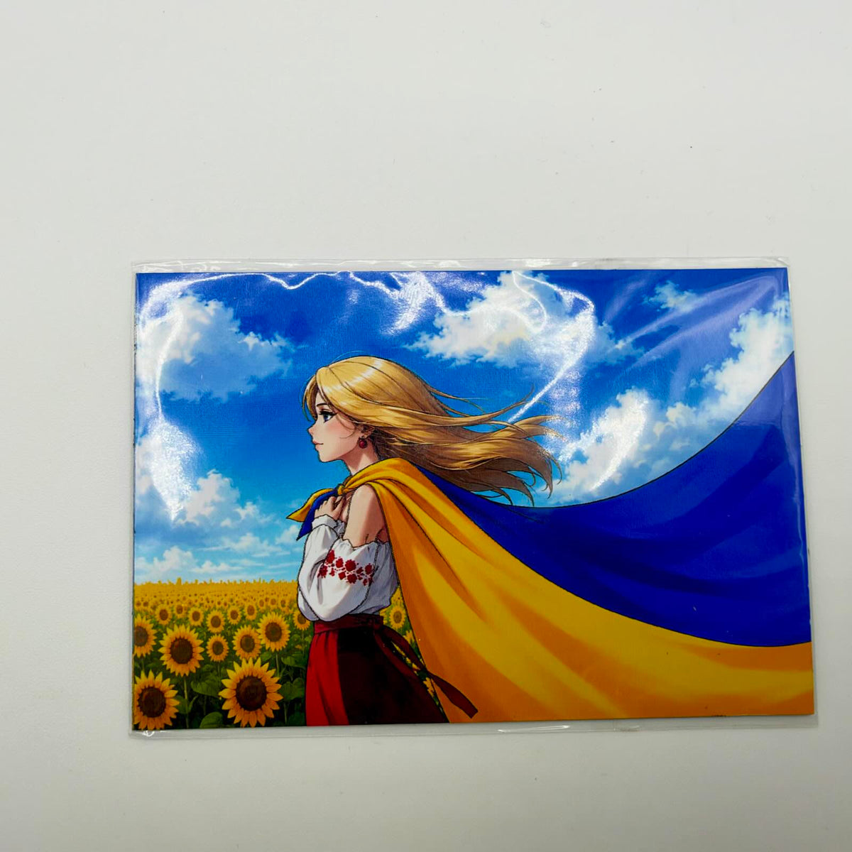 Fridge magnet showing a blonde woman in a white embroidered blouse amid sunflowers, with a Ukrainian flag flowing from her shoulders.