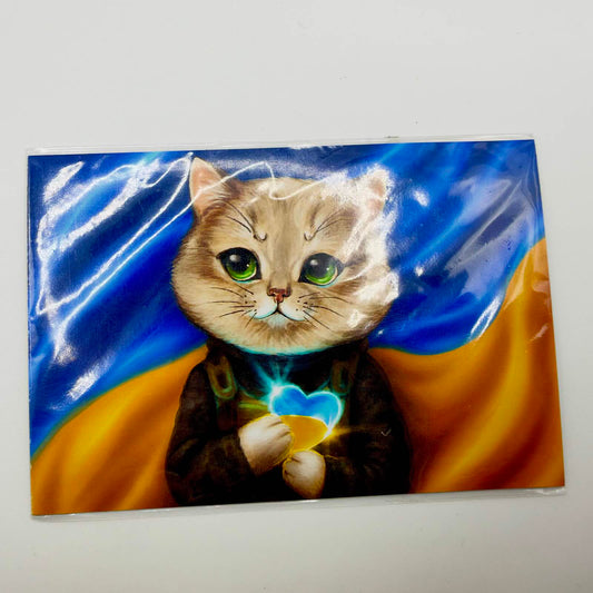 Fridge magnet showing a green-eyed cat in military-style clothing holding a glowing blue and yellow heart against a Ukrainian flag.