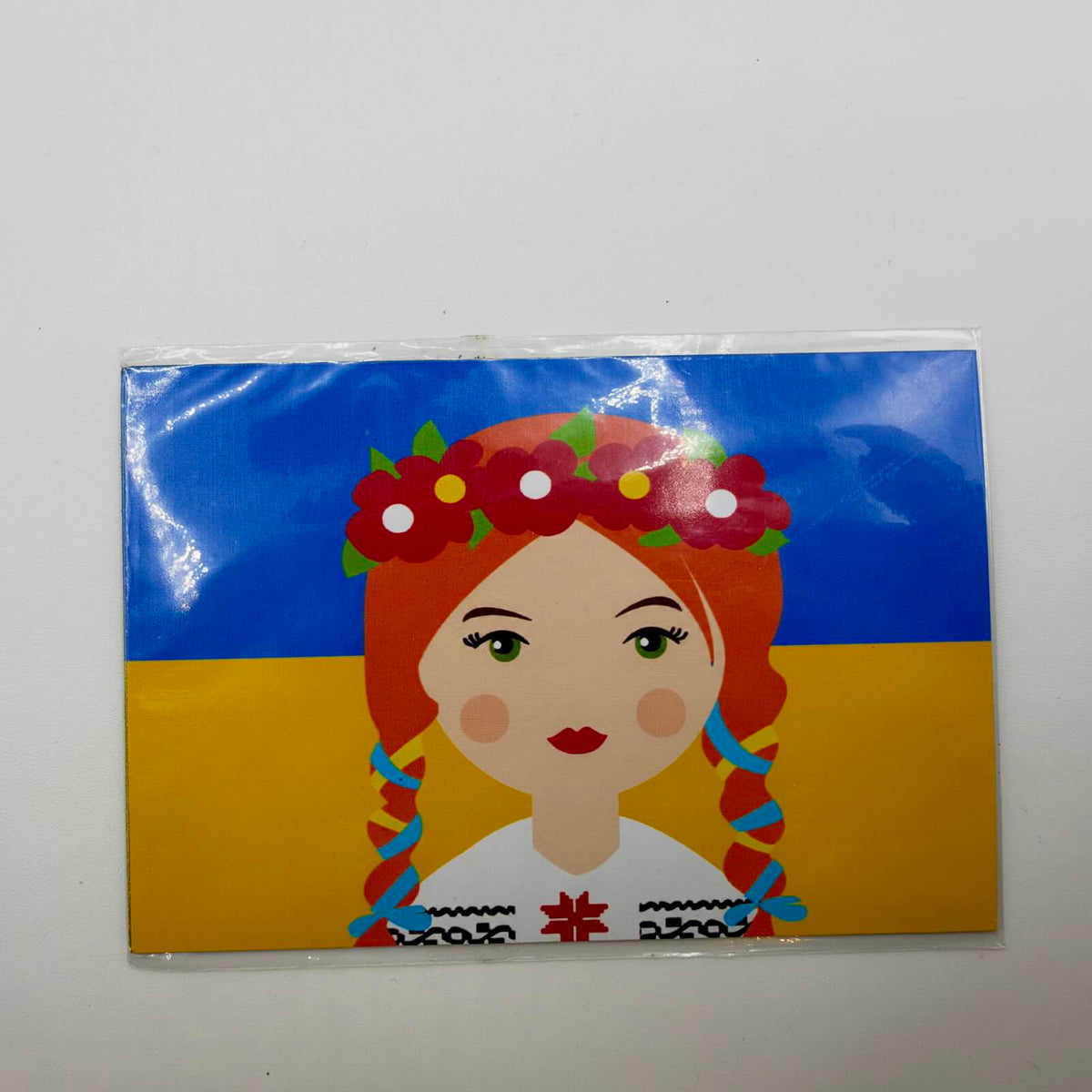 Large rectangular fridge magnet showing a red-haired girl with plaits, a red flower crown and traditional blouse against a Ukrainian flag.