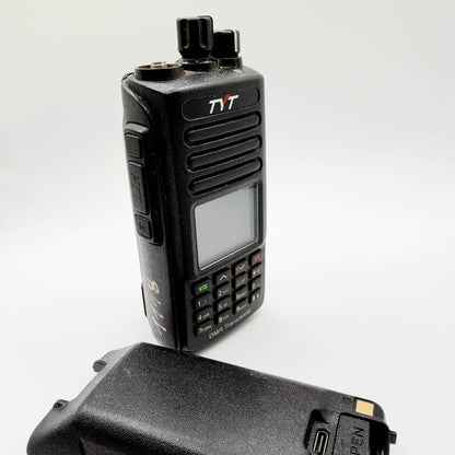 Black TYT handheld digital radio with keypad, missing antenna and detached battery on a white background.