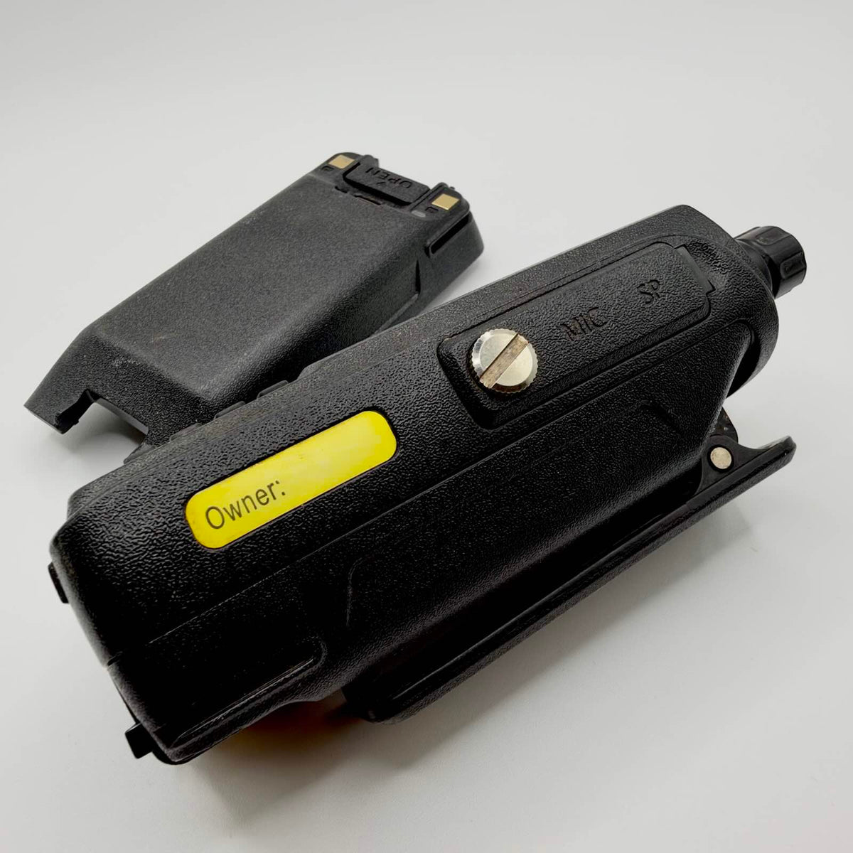 TYT radio showing its microphone and speaker connector cover, yellow owner label and belt clip beside the battery.