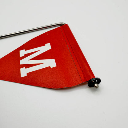 Close-up of the red mine warning flag showing its white “М”, stitched sleeve and black retaining fitting on the metal support.