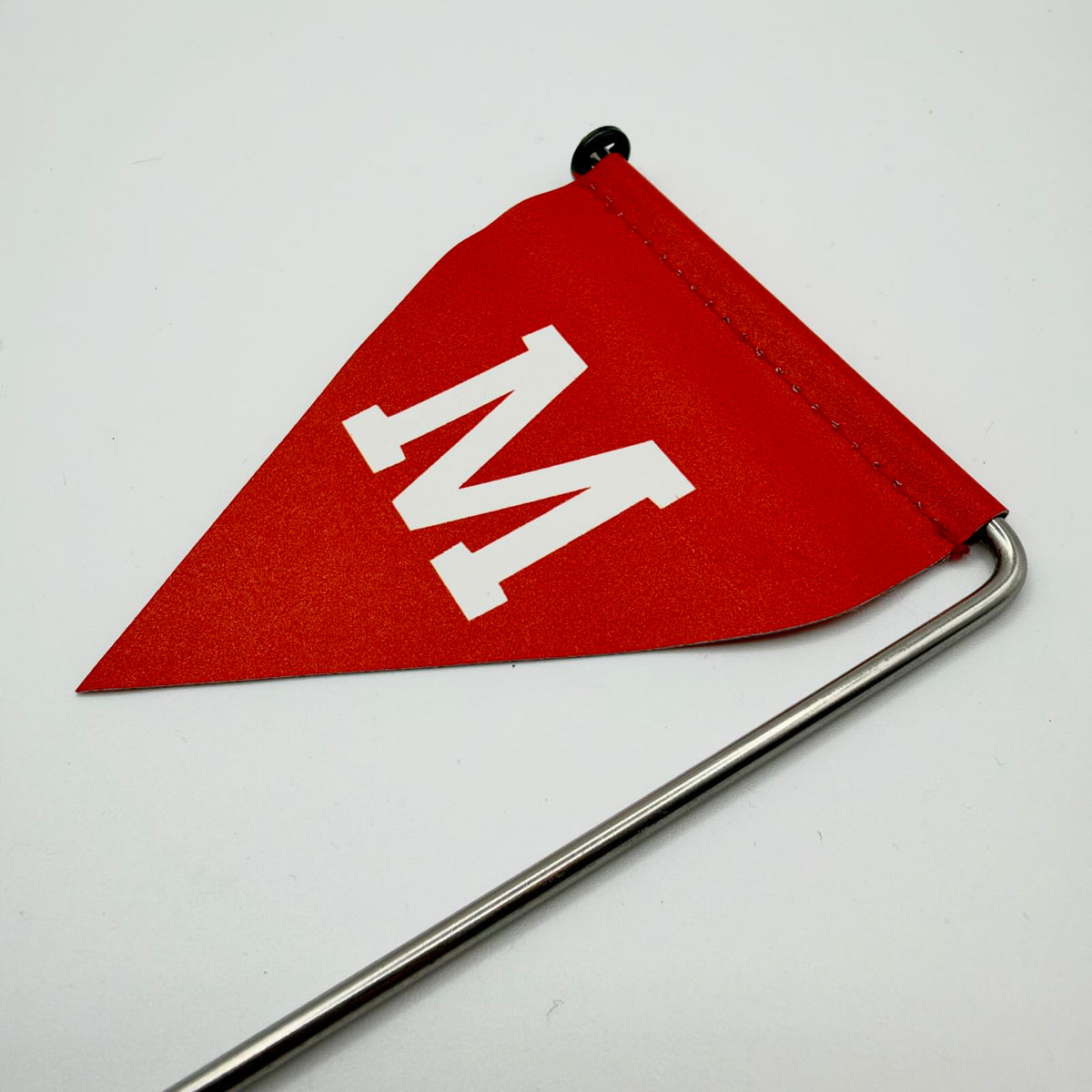 Red triangular mine warning flag with a large white “М”, showing the stitched upper edge and bent metal stake supporting the flag.