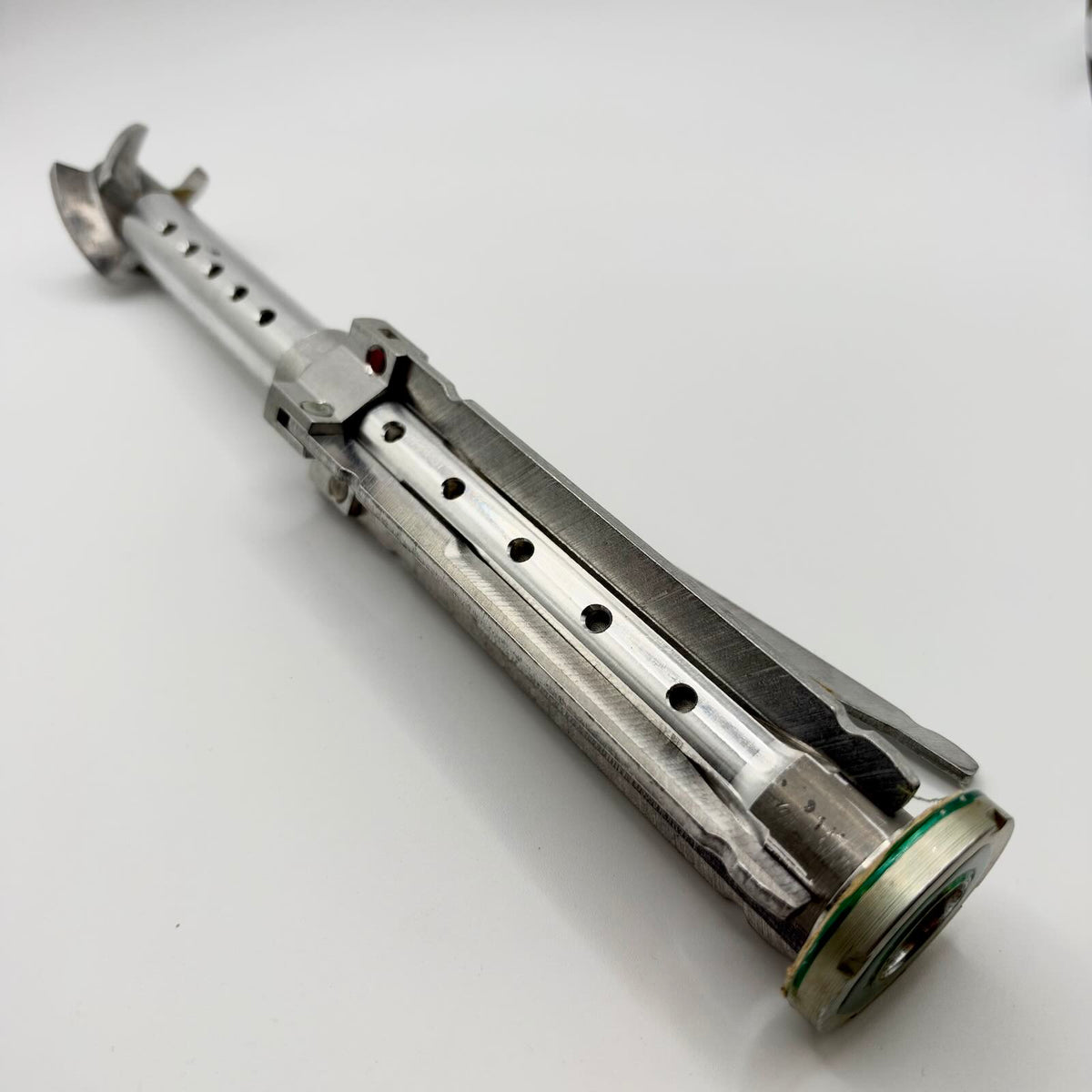 Inert RPG-7-pattern tail stabiliser assembly with four fins folded against its perforated metal tube, shown diagonally on a white background.