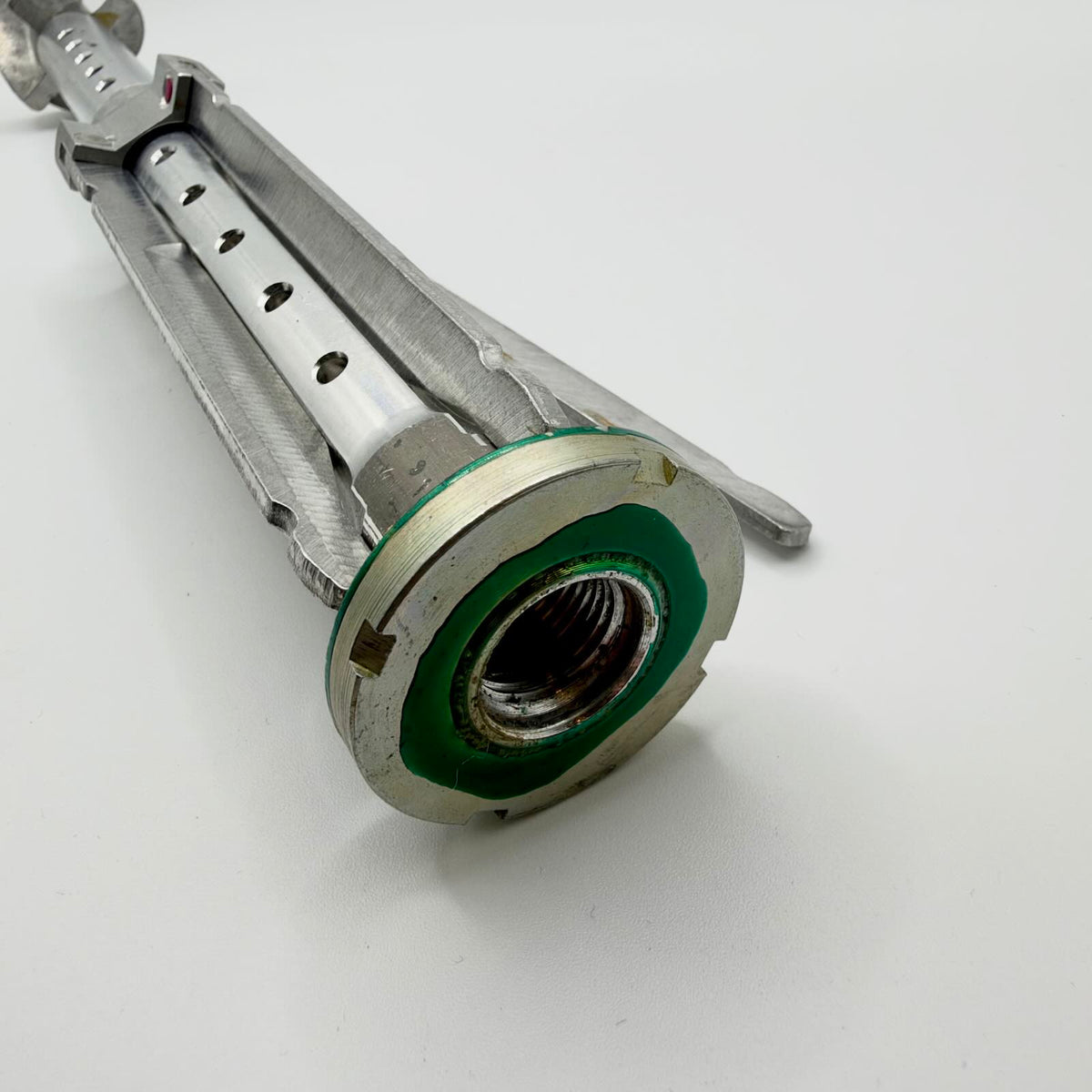 Close-up of the stabiliser’s circular threaded collar, green finish traces and folded fins alongside the perforated central tube.