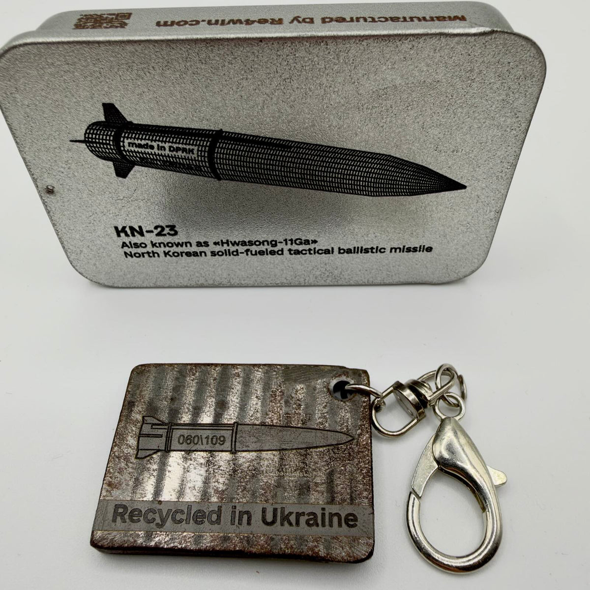 Dark metal fragment keyring with a missile illustration and “Recycled in Ukraine” inscription, attached to a silver-tone swivel and lobster clasp.
