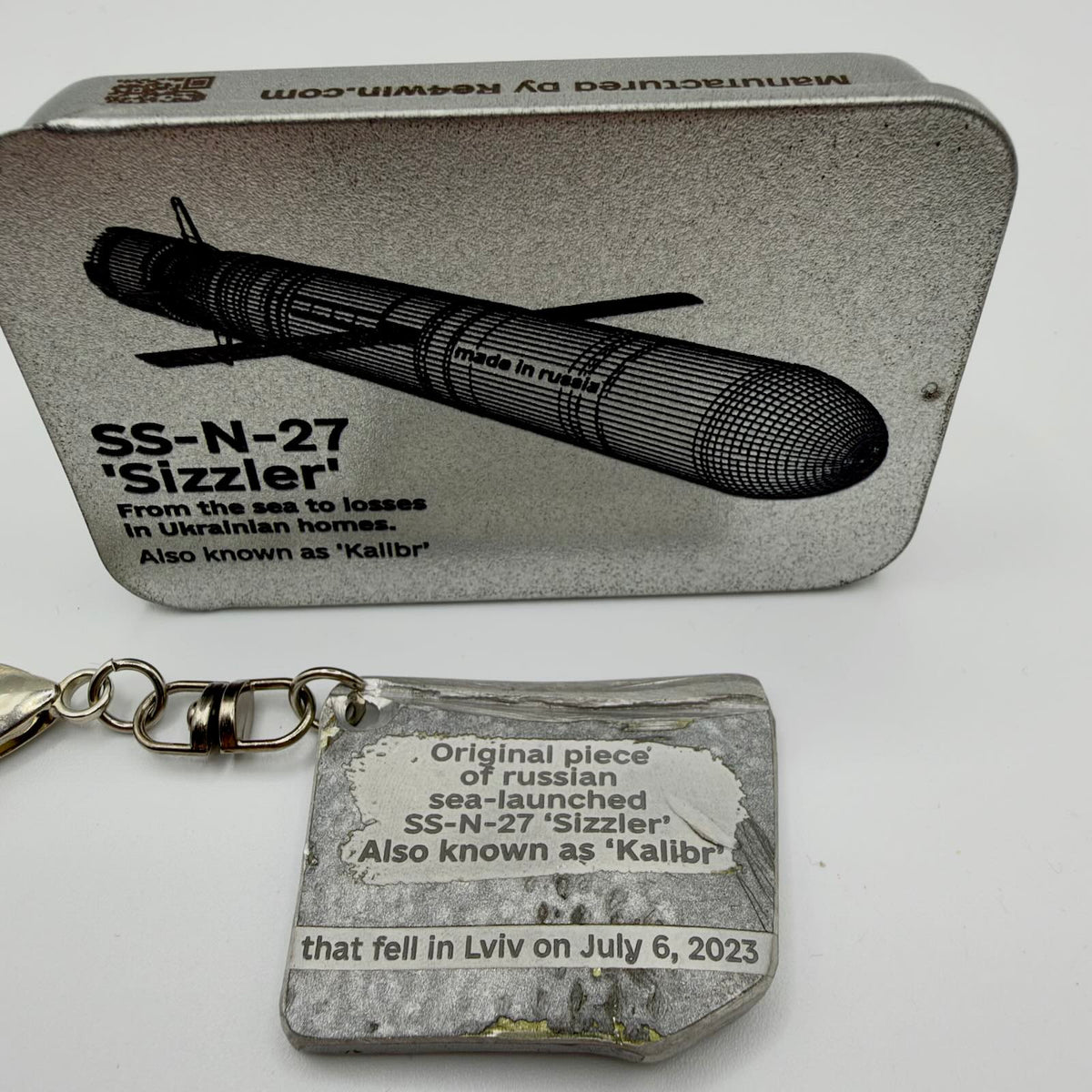 Kalibr missile fragment keyring inscribed with Lviv, 6 July 2023, pictured beside a RE4WIN tin labelled SS-N-27 “Sizzler”.