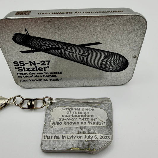 Kalibr missile fragment keyring inscribed with Lviv, 6 July 2023, pictured beside a RE4WIN tin labelled SS-N-27 “Sizzler”.