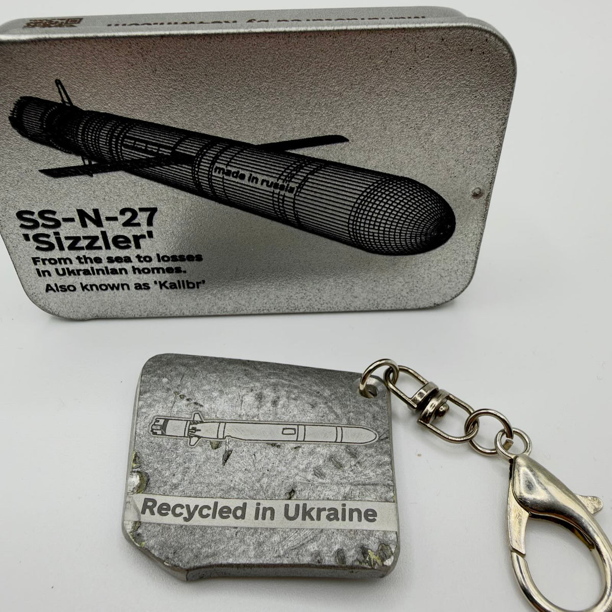Silver-grey missile fragment keyring with a missile illustration, “Recycled in Ukraine” inscription, swivel connector and clasp.