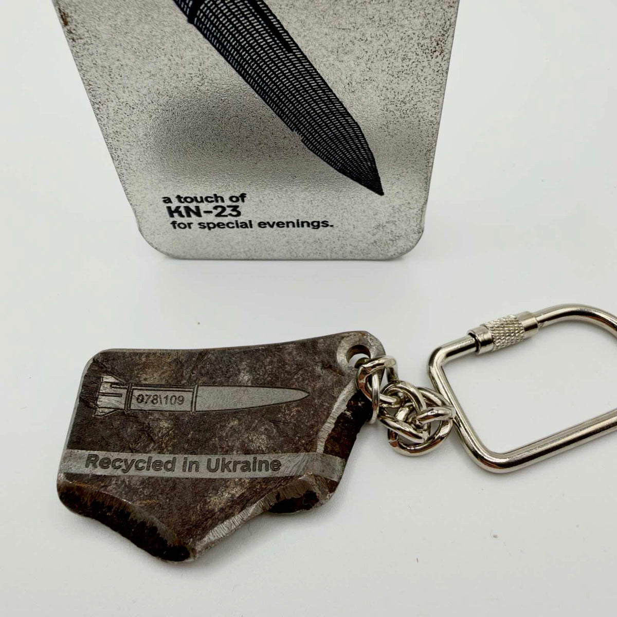 Chunky, irregular metal keyring with a missile illustration and “Recycled in Ukraine” inscription, attached to a chain and screw-closure fitting.