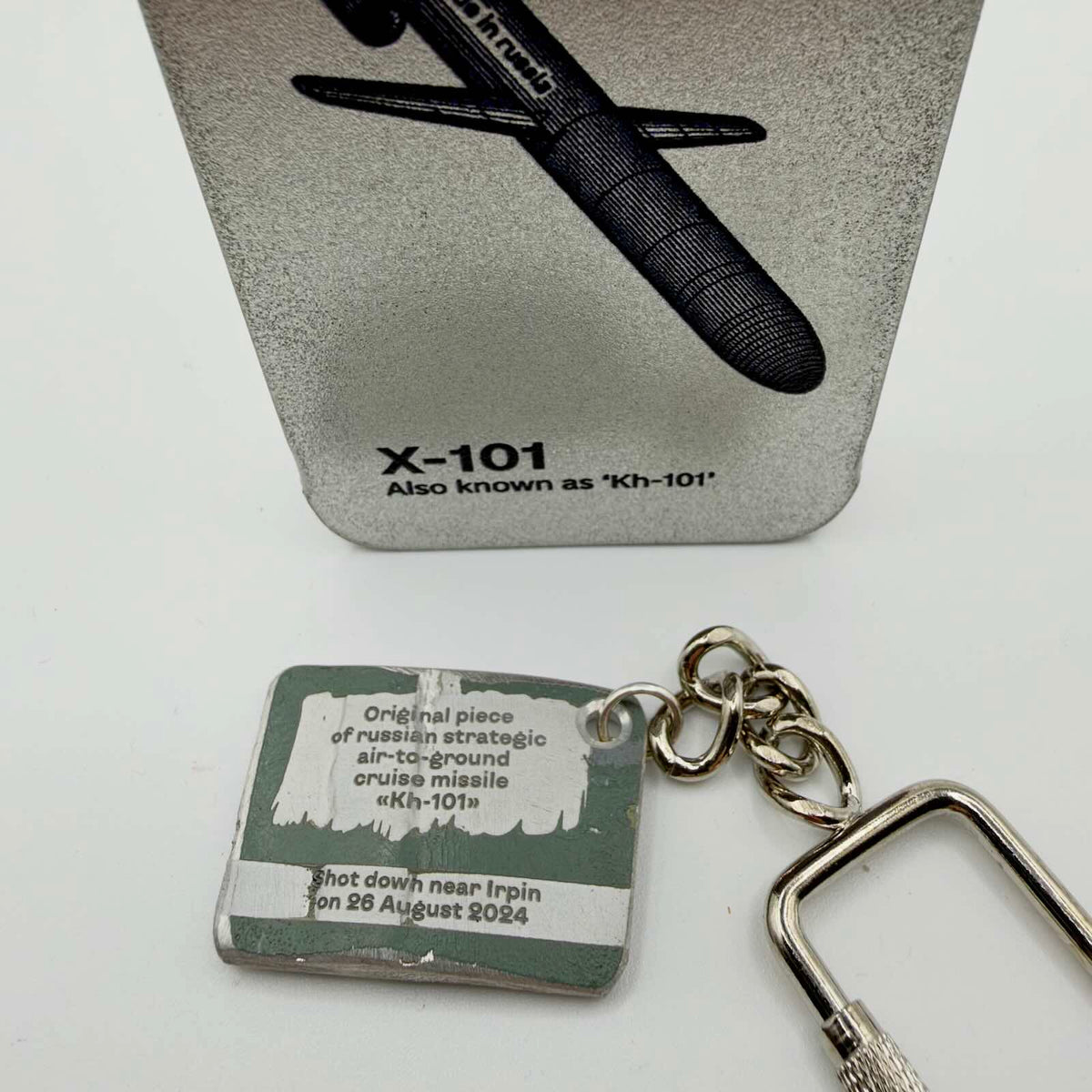 RE4WIN missile fragment keyring with an inscription identifying a Kh-101 shot down near Irpin on 26 August 2024, beside an X-101 display card.