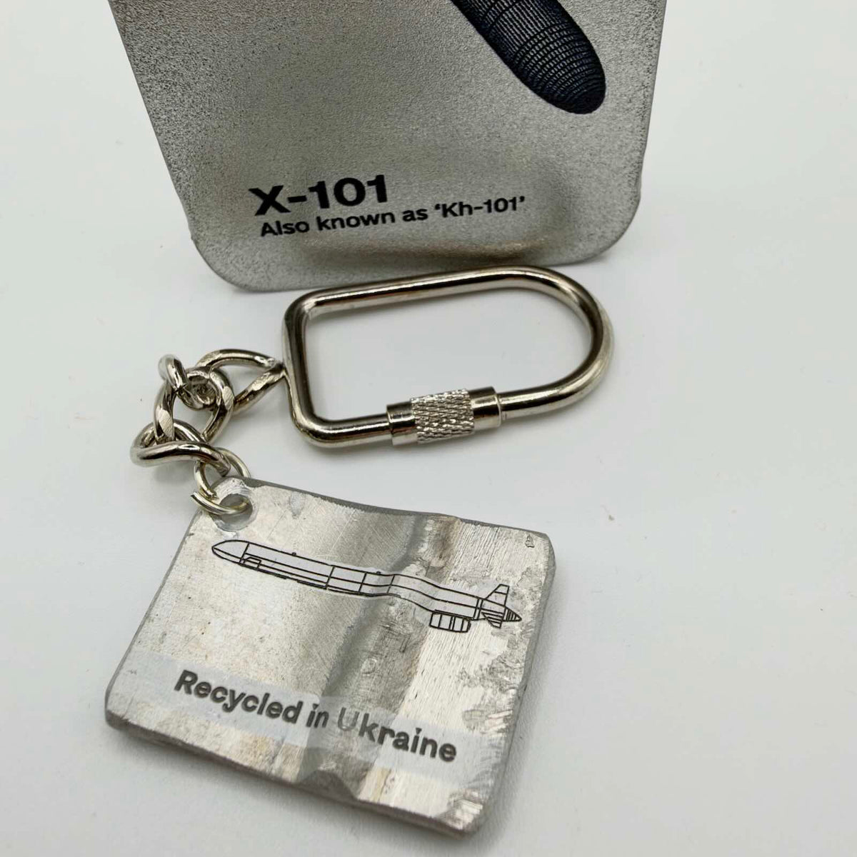 Metal missile fragment keyring with a missile outline and “Recycled in Ukraine” inscription, attached to a short chain and screw-closure fitting.