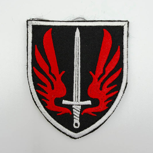 Black shield-shaped embroidered patch featuring an upright silver sword between two stylised red wings, with a silver border.
