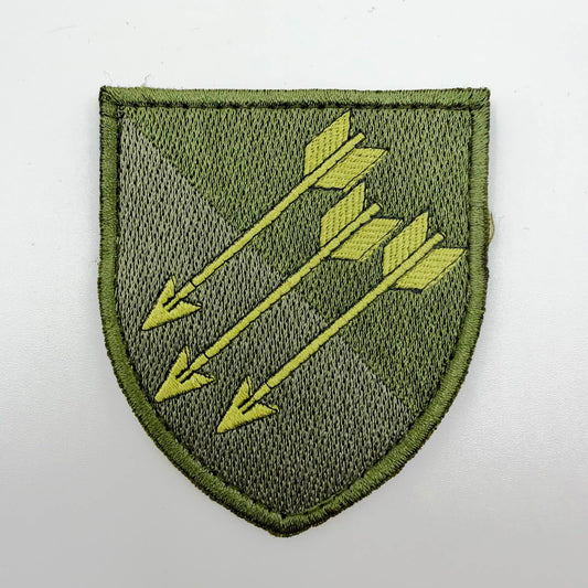 Olive-green shield-shaped embroidered patch with three parallel khaki arrows outlined in black, pointing diagonally towards the lower left.