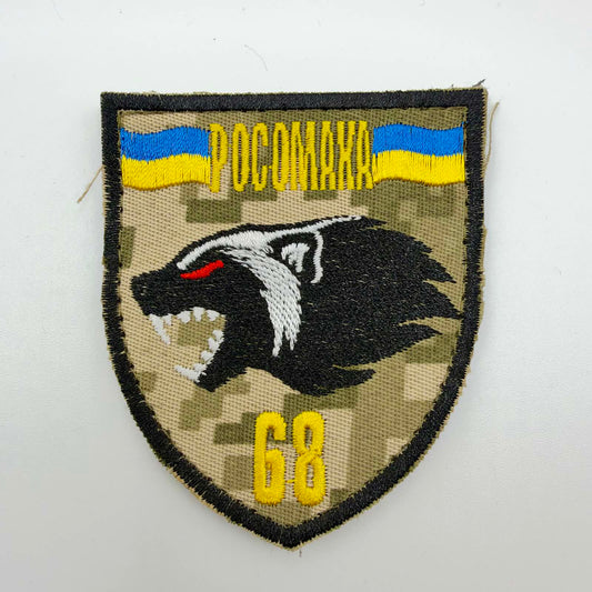 Shield-shaped camouflage patch with a black border, snarling black-and-white wolverine with a red eye, two Ukrainian flags, yellow “РОСОМАХА” lettering and the number 68.